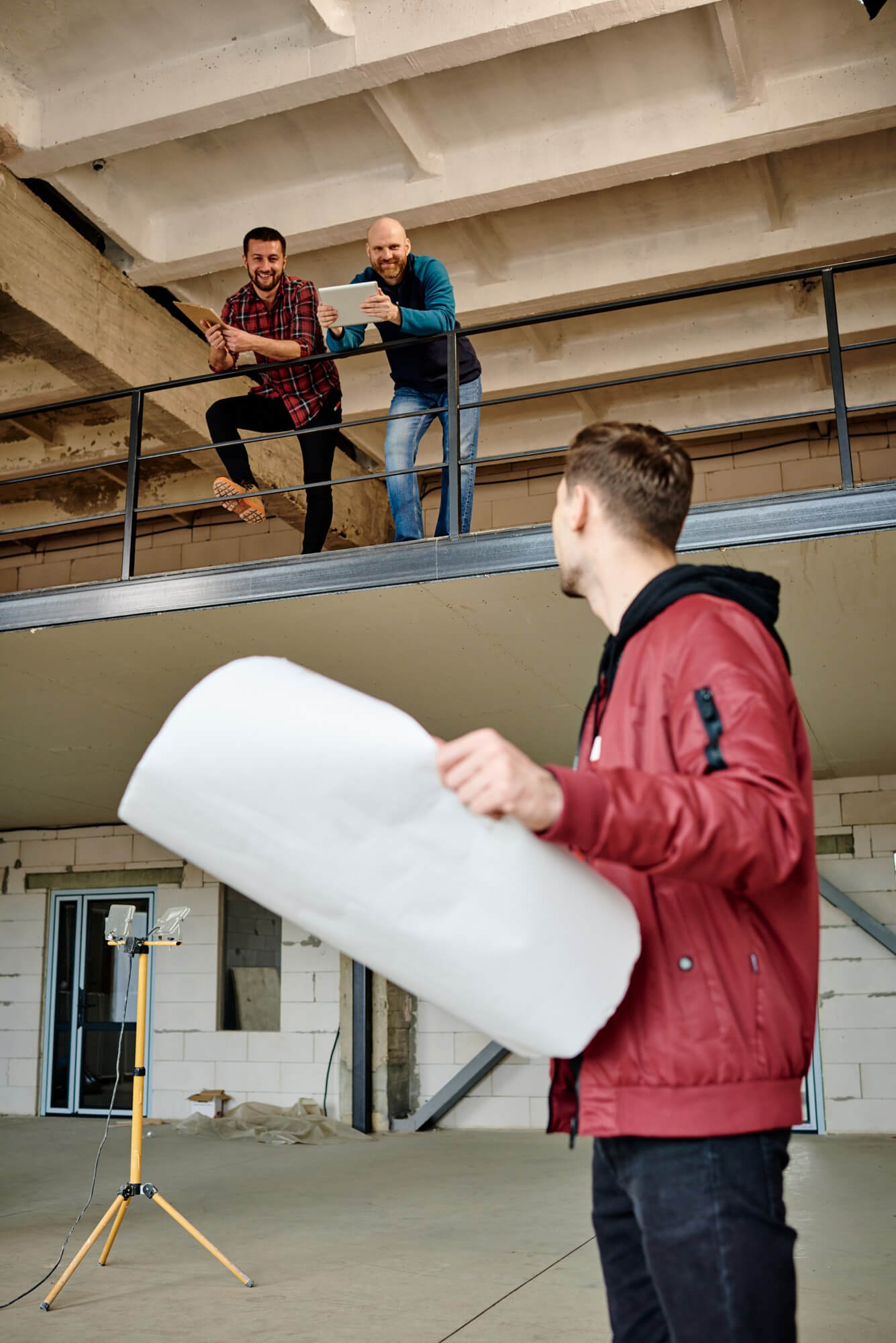 young-man-with-blueprint-standing-first-floor-unfinished-building-consulting-with-colleagues-second-floor-meeting-2
